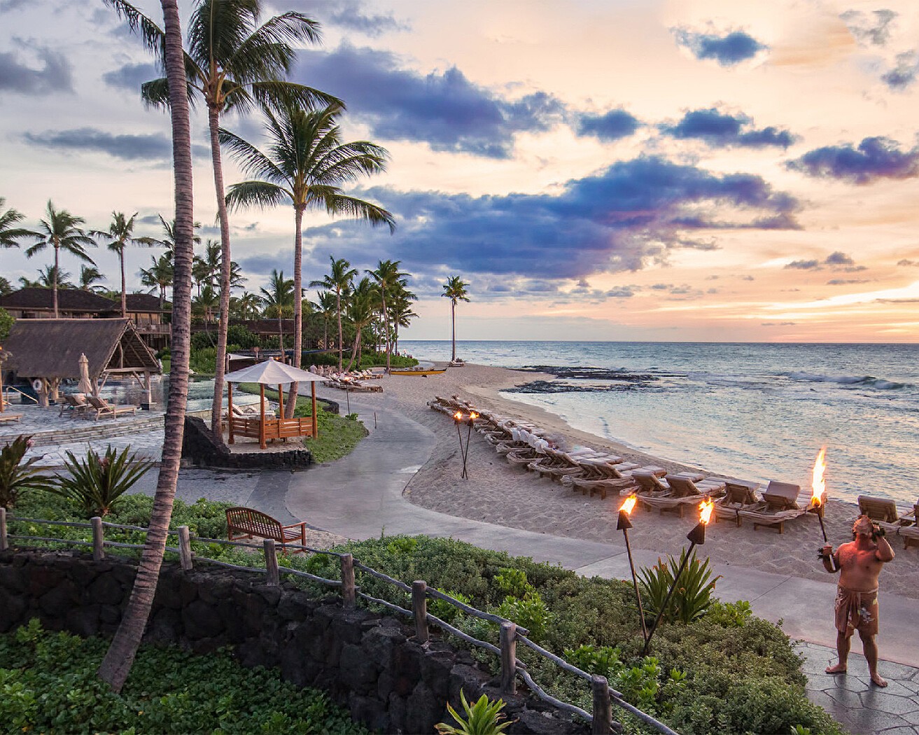 Torches lit along the beach at sunset at Four Seasons Resort Hualalai